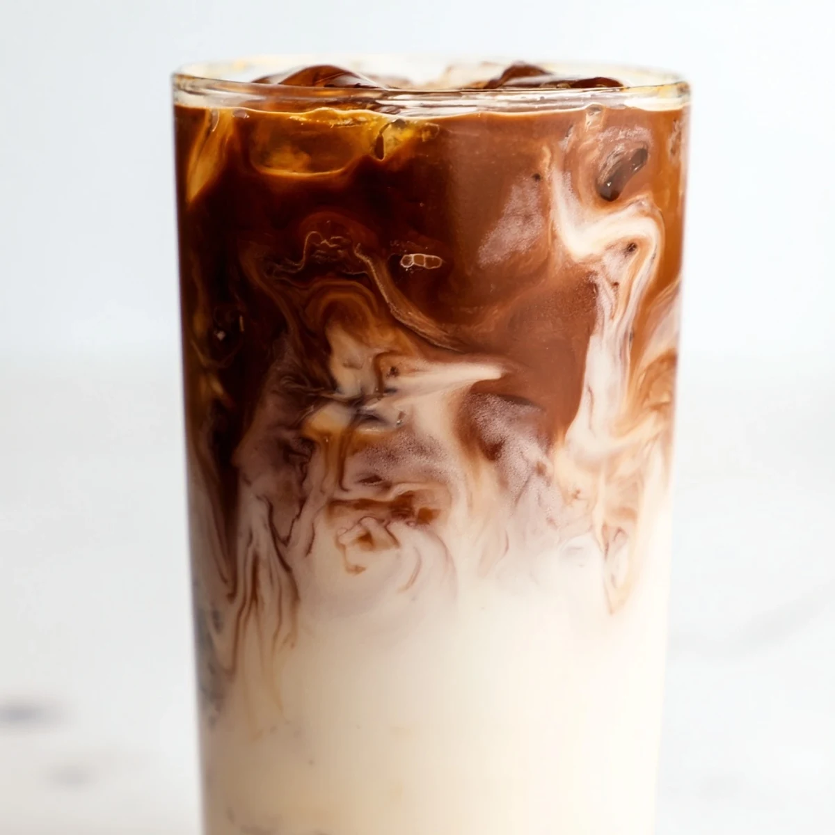 A freshly prepared glass of the Milo Ice Latte Hack with a straw, garnished with a light dusting of Milo powder.