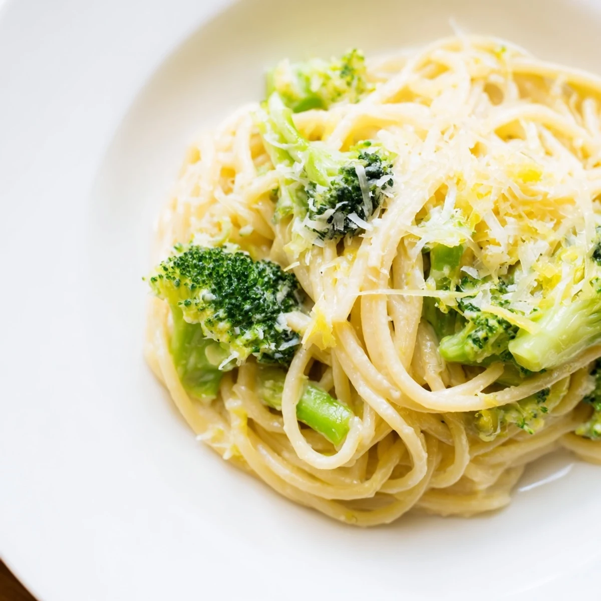 A close-up of One-Pot Lemon Broccoli Pasta in a white bowl, with bright green broccoli florets and silky sauce clinging to each strand.  
