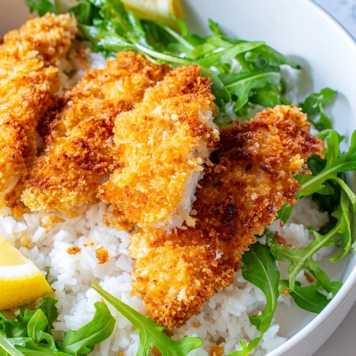 A finished Crispy Parmesan Chicken Cutlet Bowl with lemon wedges for serving.