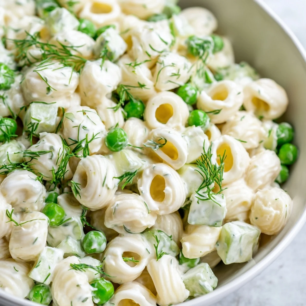 A vibrant bowl of creamy dill pickle pasta salad, featuring ditalini, peas, and crunchy pickle chunks, ready for a picnic.