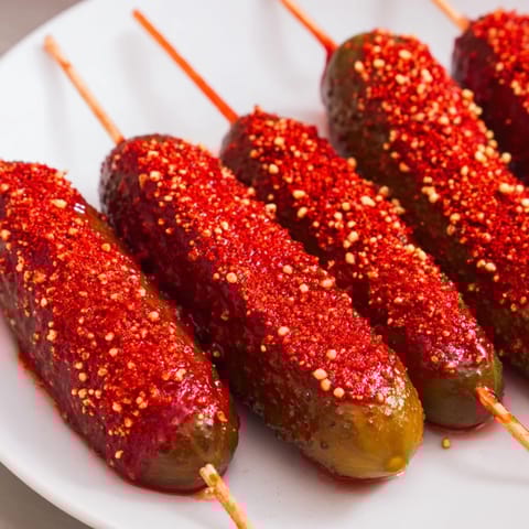 Bright red Chamoy-Tajín pickle sticks, with a dusting of Tajín, offer a zesty, sweet-spicy crunch.