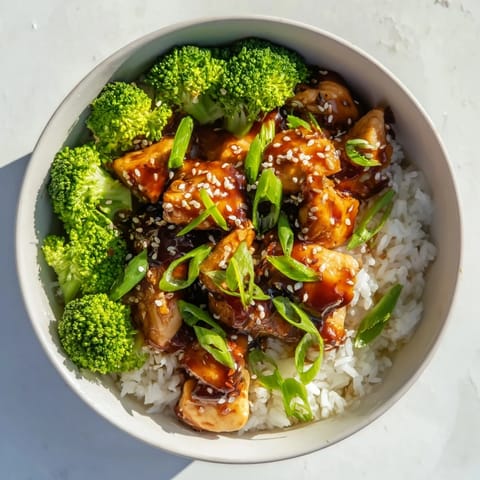 A close-up view of glistening sweet chili chicken pieces served in a bowl with rice and green onions.