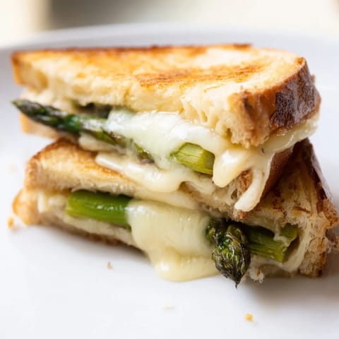 A close-up view of an Asparagus & Brie Grilled Cheese showcasing charred green stalks and gooey cheese on crusty bread.  