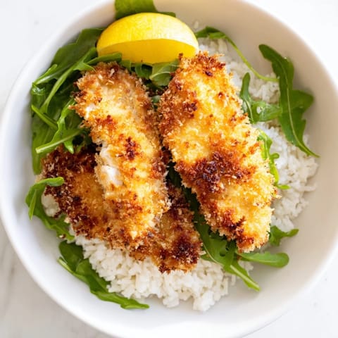 Sliced Parmesan chicken cutlets layered over warm rice and fresh arugula.  
