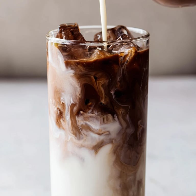 A hand holding a tall glass of the refreshing homemade Milo Ice Latte Hack, perfect for a quick afternoon energy boost.